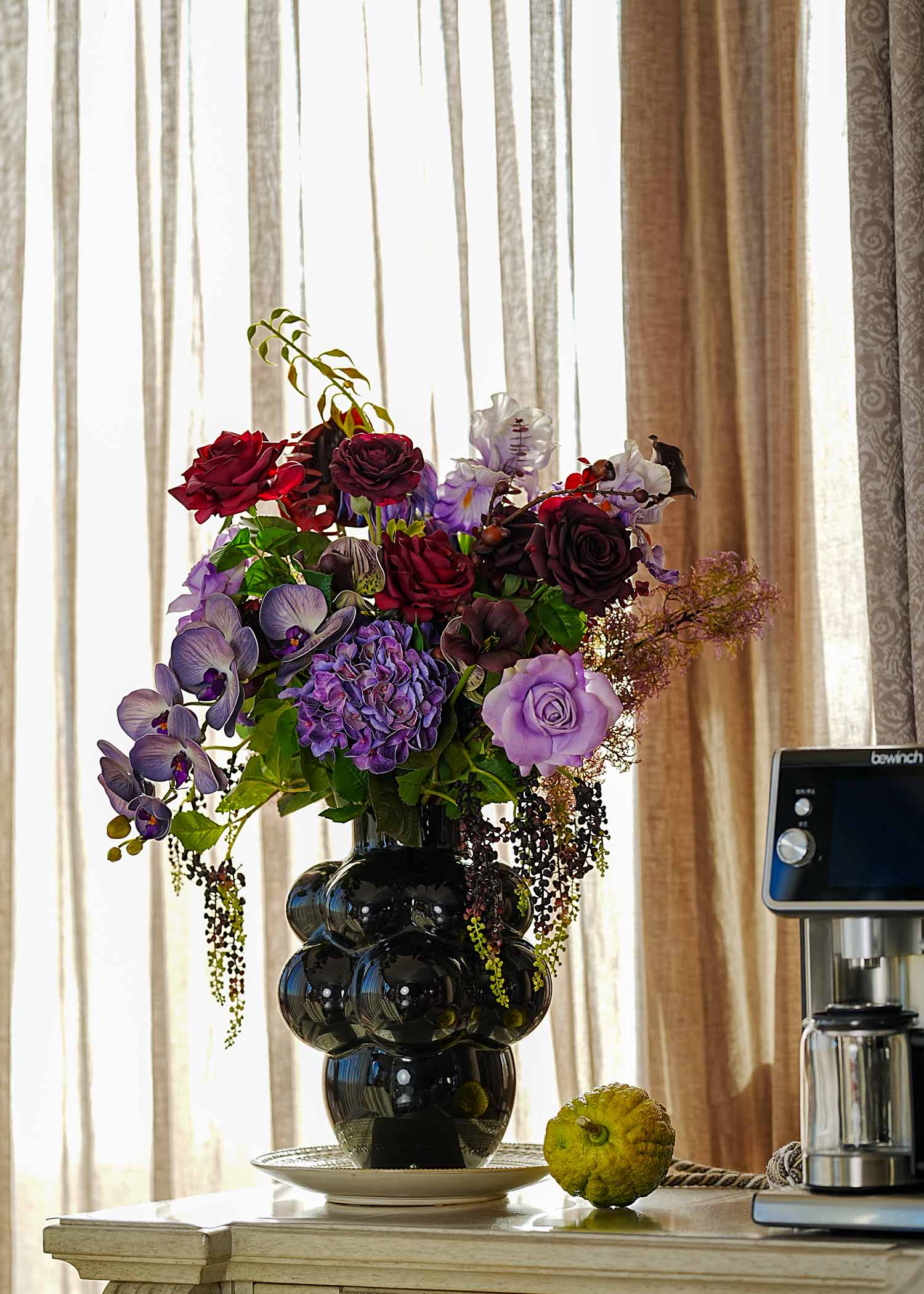 Amethyst and burgundy faux floral bouquet styled in a modern black vase for contemporary interior decoration.