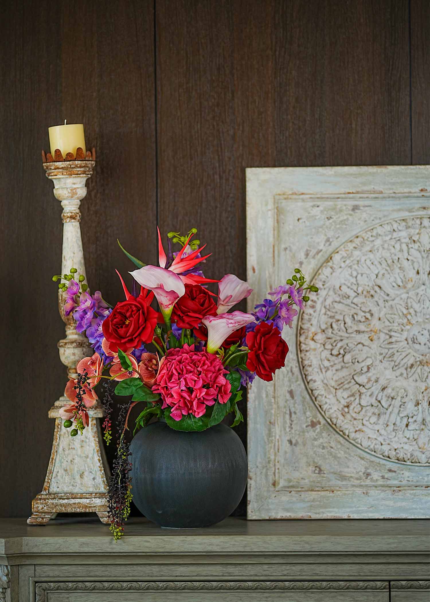 Crimson Paradise faux floral arrangement with red roses and calla lilies placed on a dining table beside a vintage candle holder.
