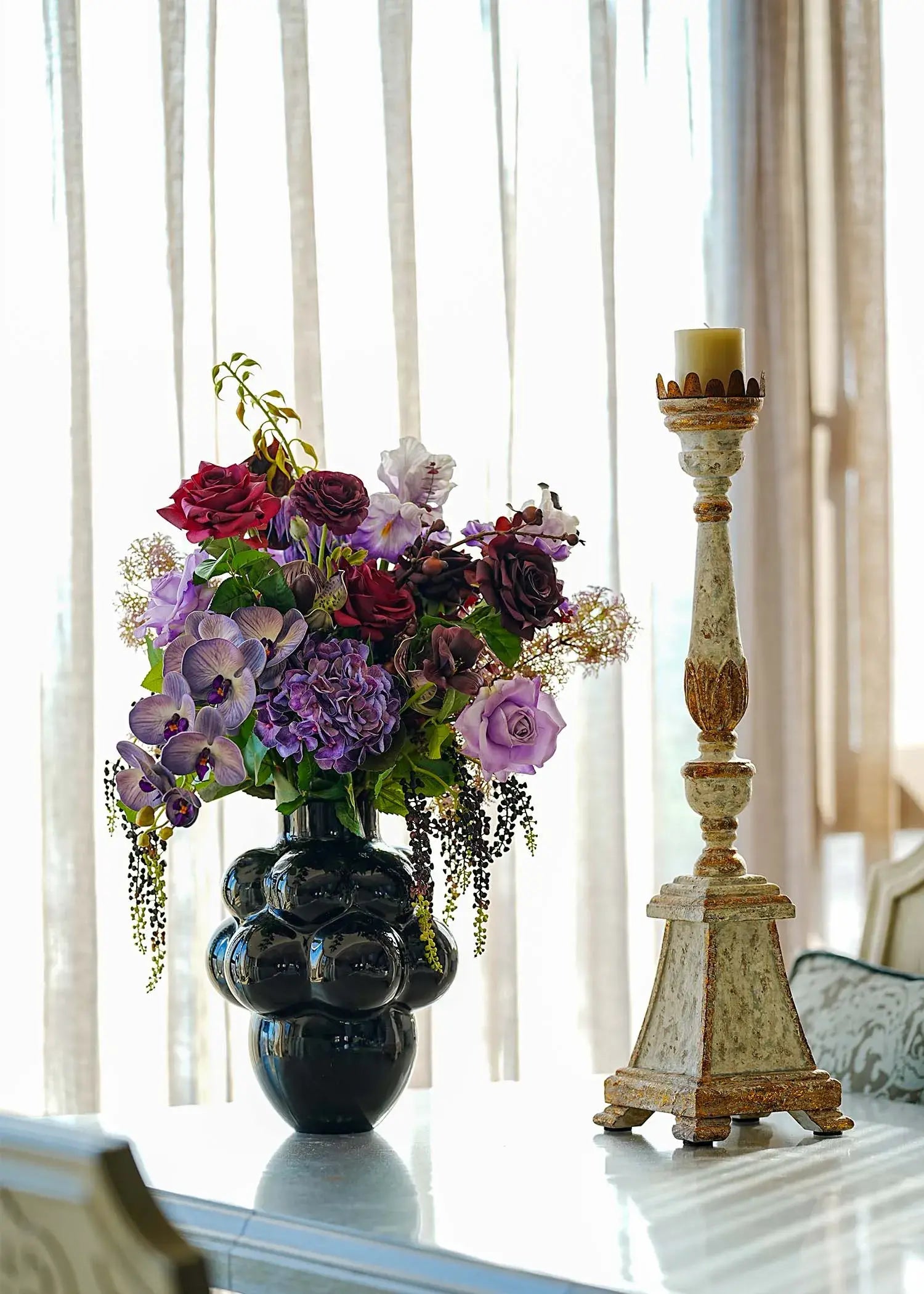 Deep purple and red artificial flower centerpiece with orchids and roses arranged in a glossy black vase.