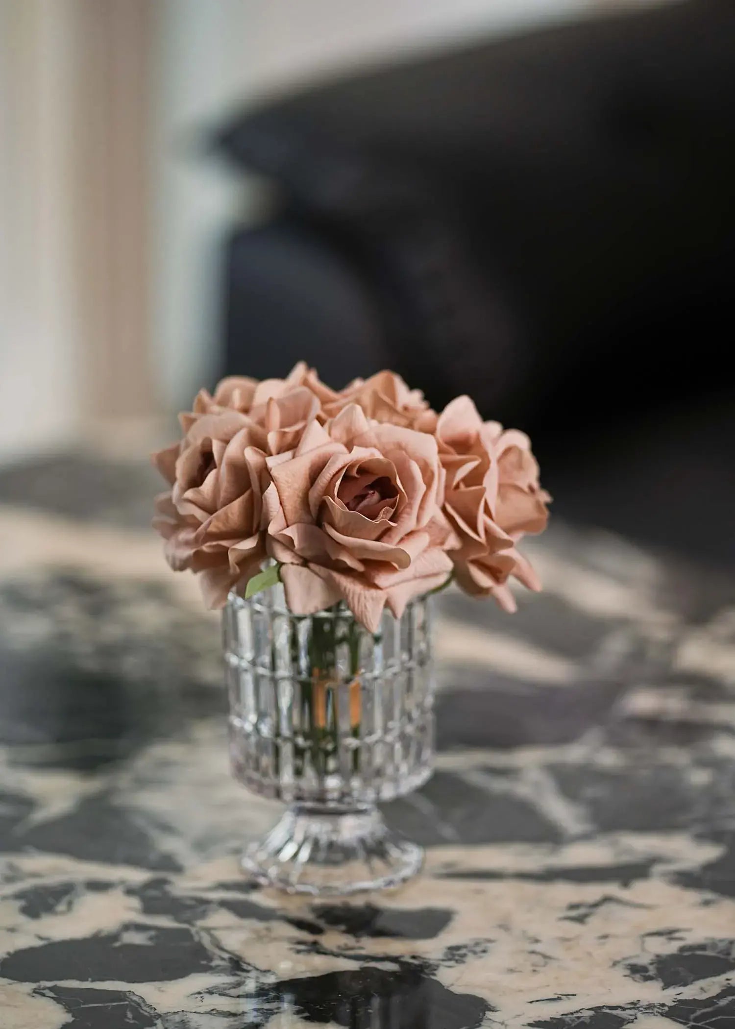 Dusty pink artificial roses arrangement in clear glass vase on white side table, minimalist interior style