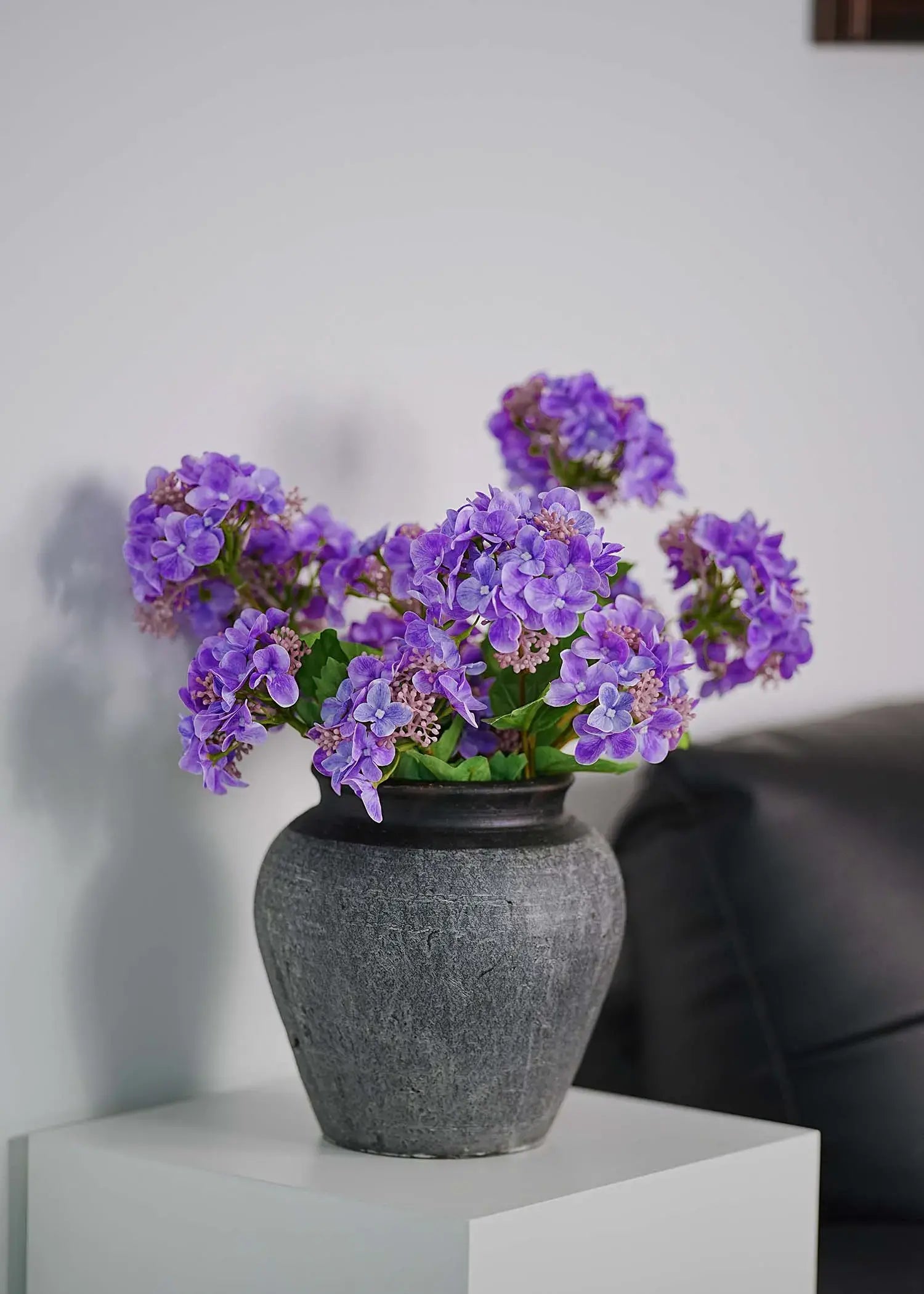 Lavender artificial hydrangeas bouquet in matte black vase on white side table, minimalist living room decoration
