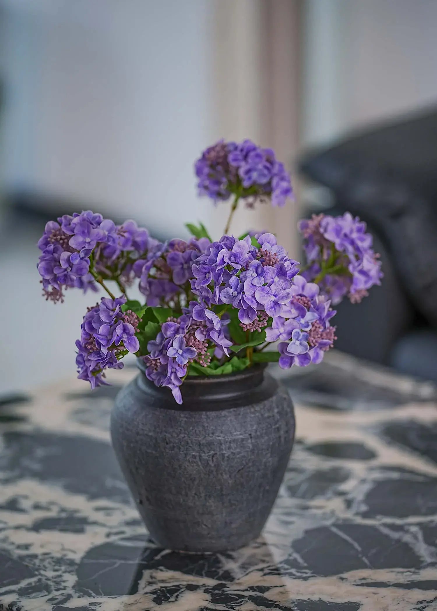 Vibrant purple hydrangea bouquet in dark ceramic vase on marble table, modern home interior accent by Everblooma