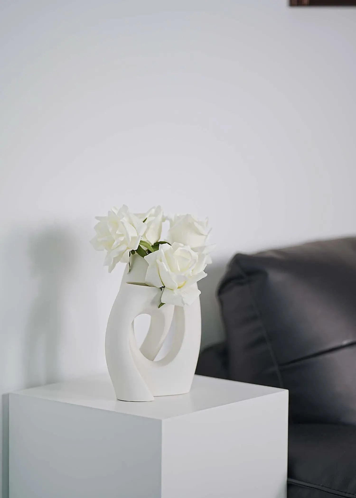 White artificial roses arrangement in abstract ceramic vase on white stand, minimalist living room decoration