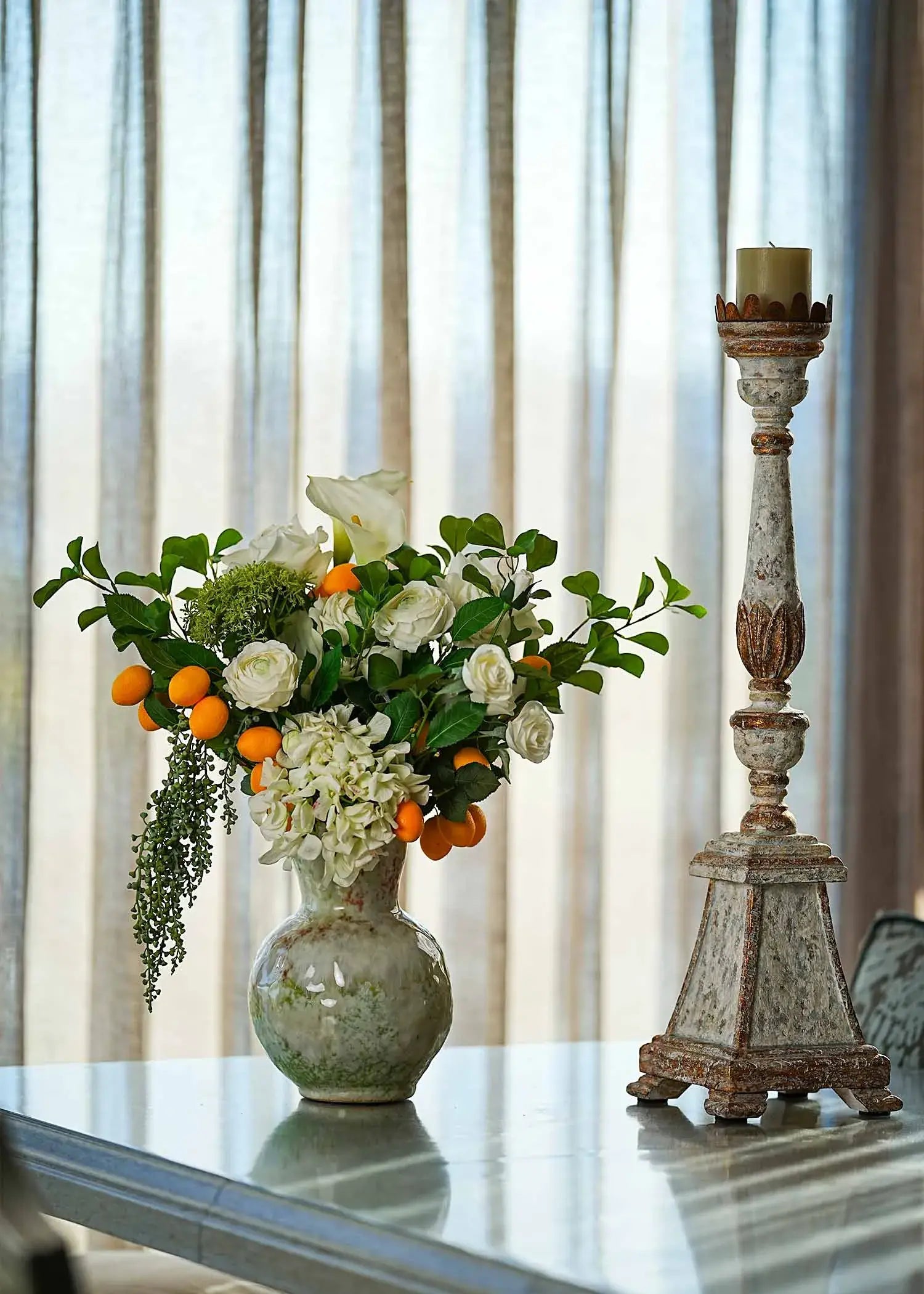 Fresh Citrus & White Roses faux floral arrangement with calla lilies, hydrangea and citrus accents in a vintage ceramic vase on a dining table.