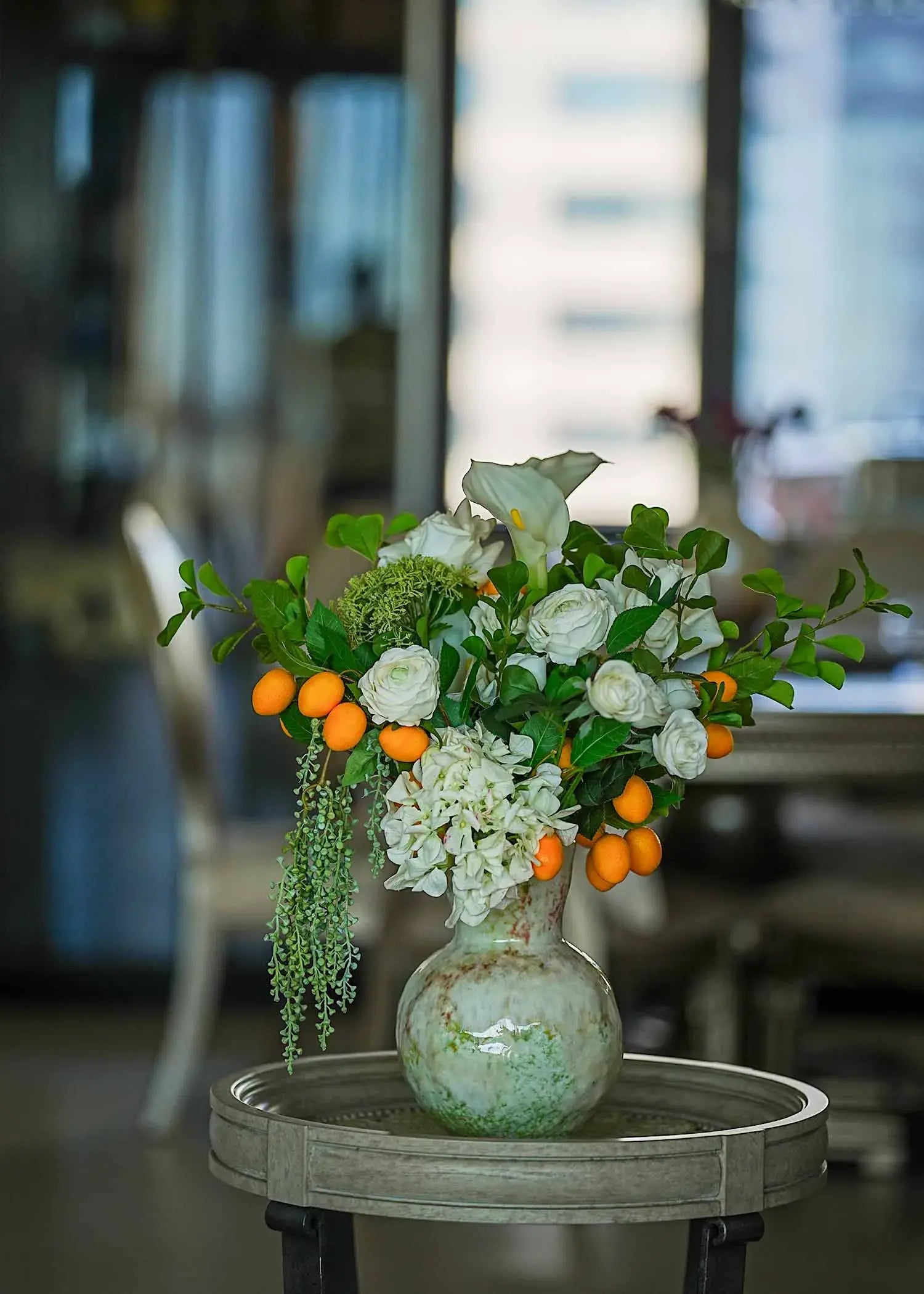 Fresh Citrus & White Roses faux floral arrangement featuring calla lilies and orange accents in a round vintage vase under soft daylight.