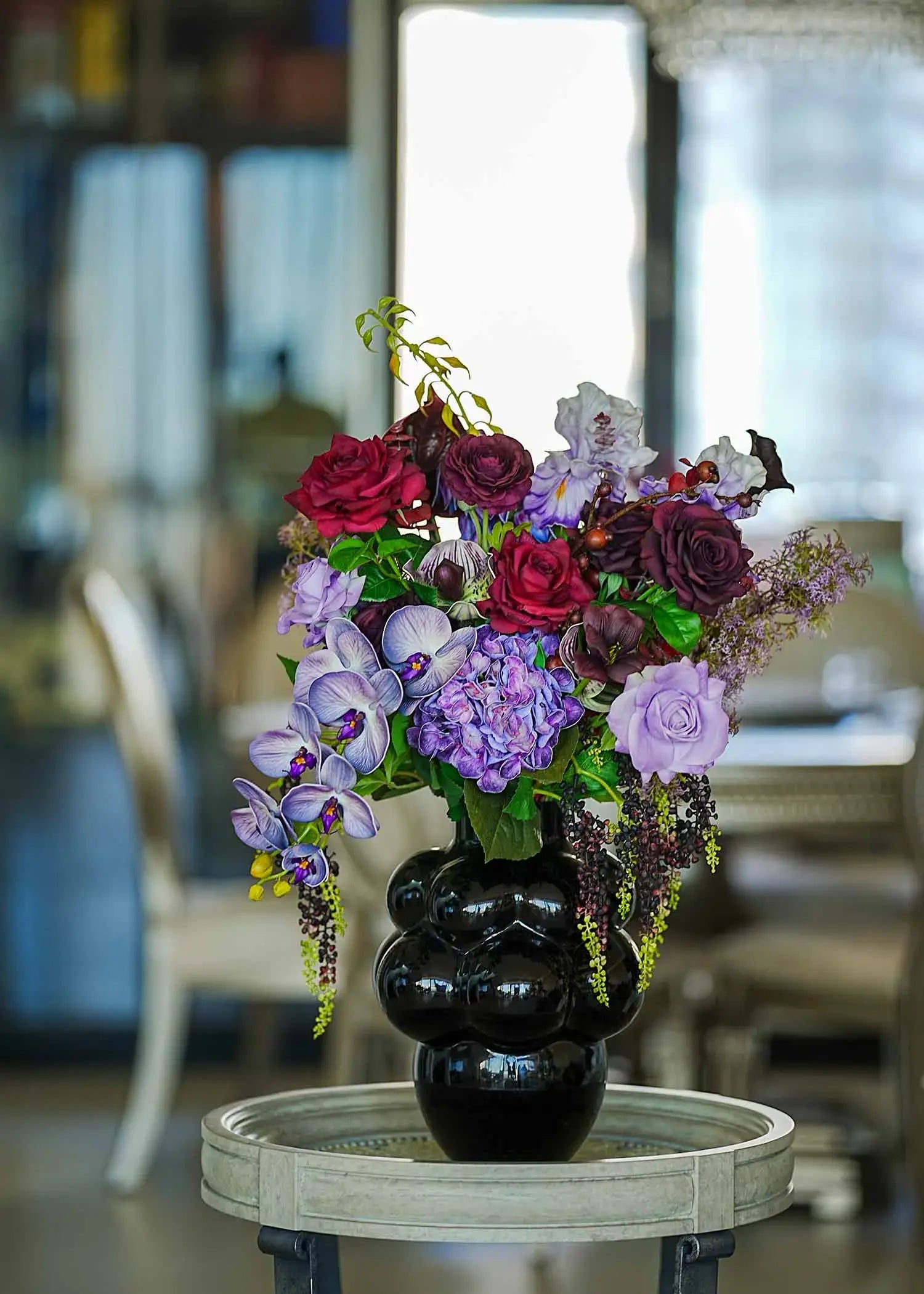 Luxury faux floral arrangement in rich purple and burgundy tones displayed on a wooden table under warm natural light.