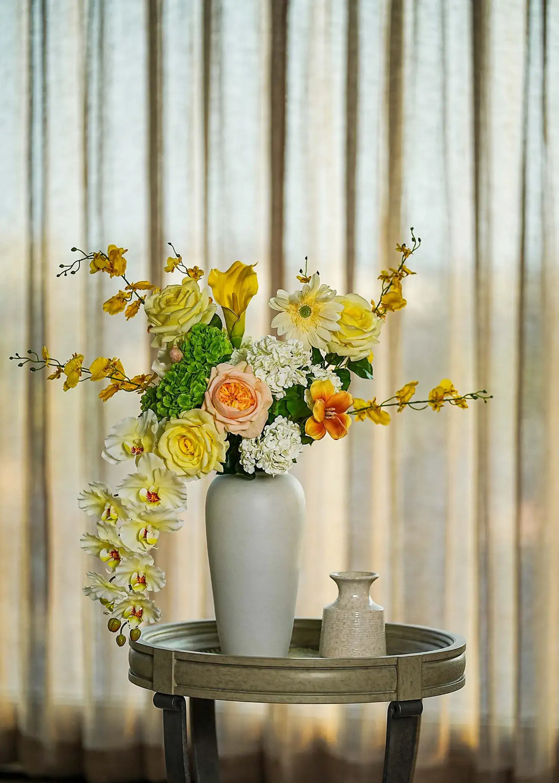 Real Touch faux floral centerpiece with roses and orchids in a tall white vase, styled on a round table with soft curtain backdrop — Everblooma elegant home décor.