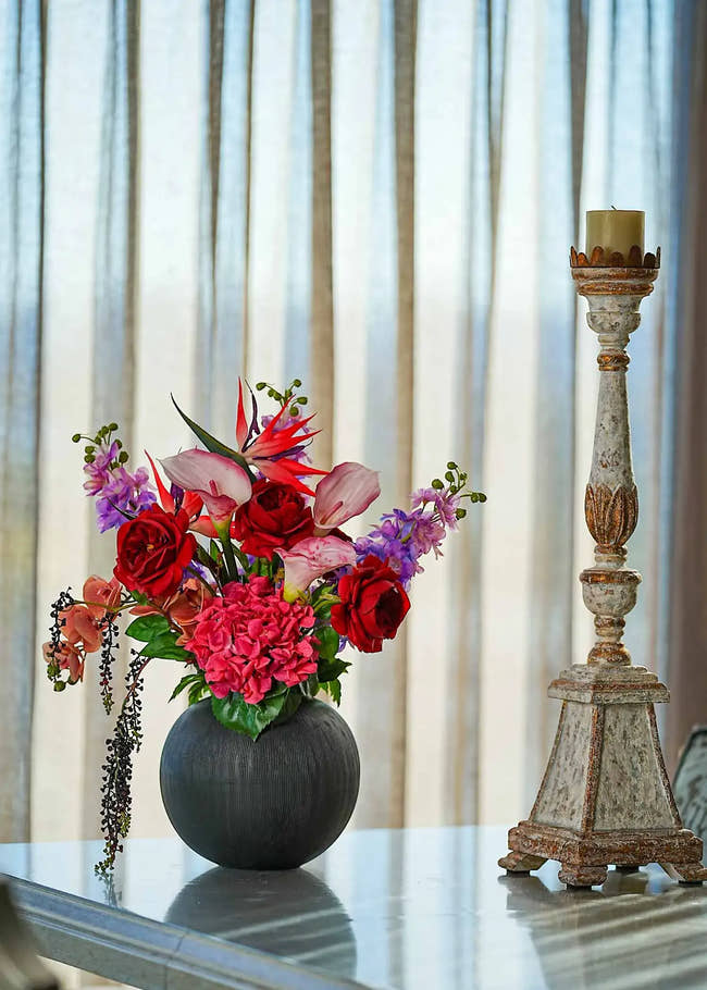 Crimson Paradise faux floral arrangement with red roses, calla lilies, and paradise birds in a black vase on a wooden console table.