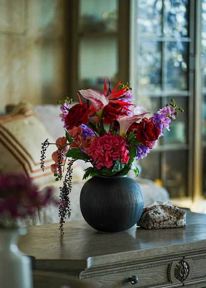 Crimson Paradise faux flower arrangement in a black vase displayed on a wooden coffee table in a cozy living room.