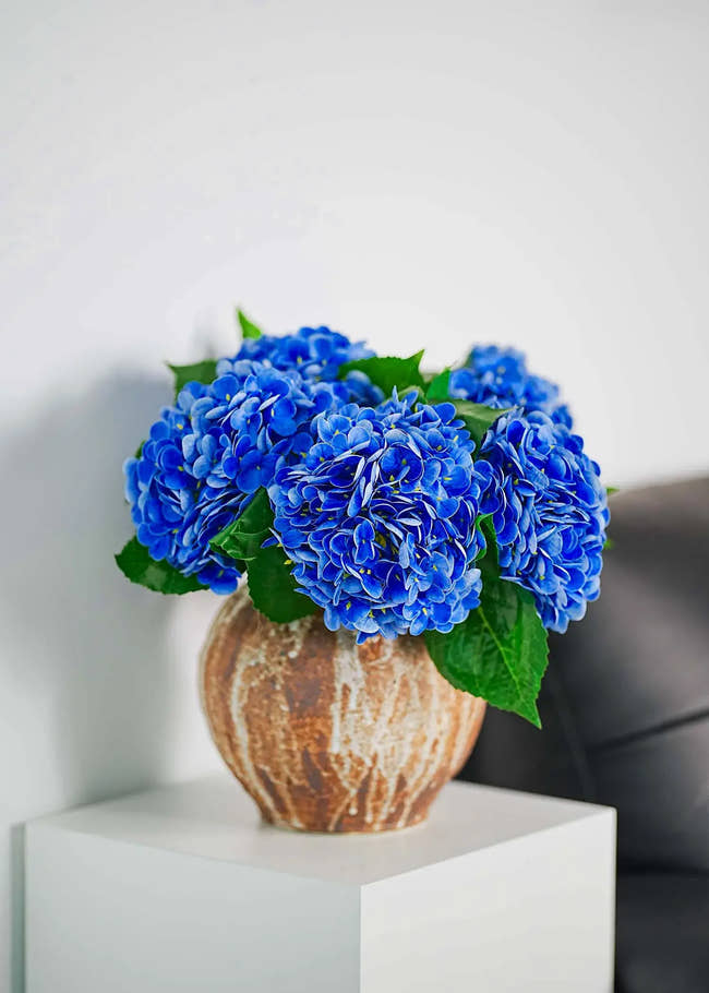 Vivid blue artificial hydrangeas bouquet in pottery vase on white side table, modern minimalist interior accent