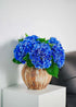 Vivid blue artificial hydrangeas bouquet in pottery vase on white side table, modern minimalist interior accent