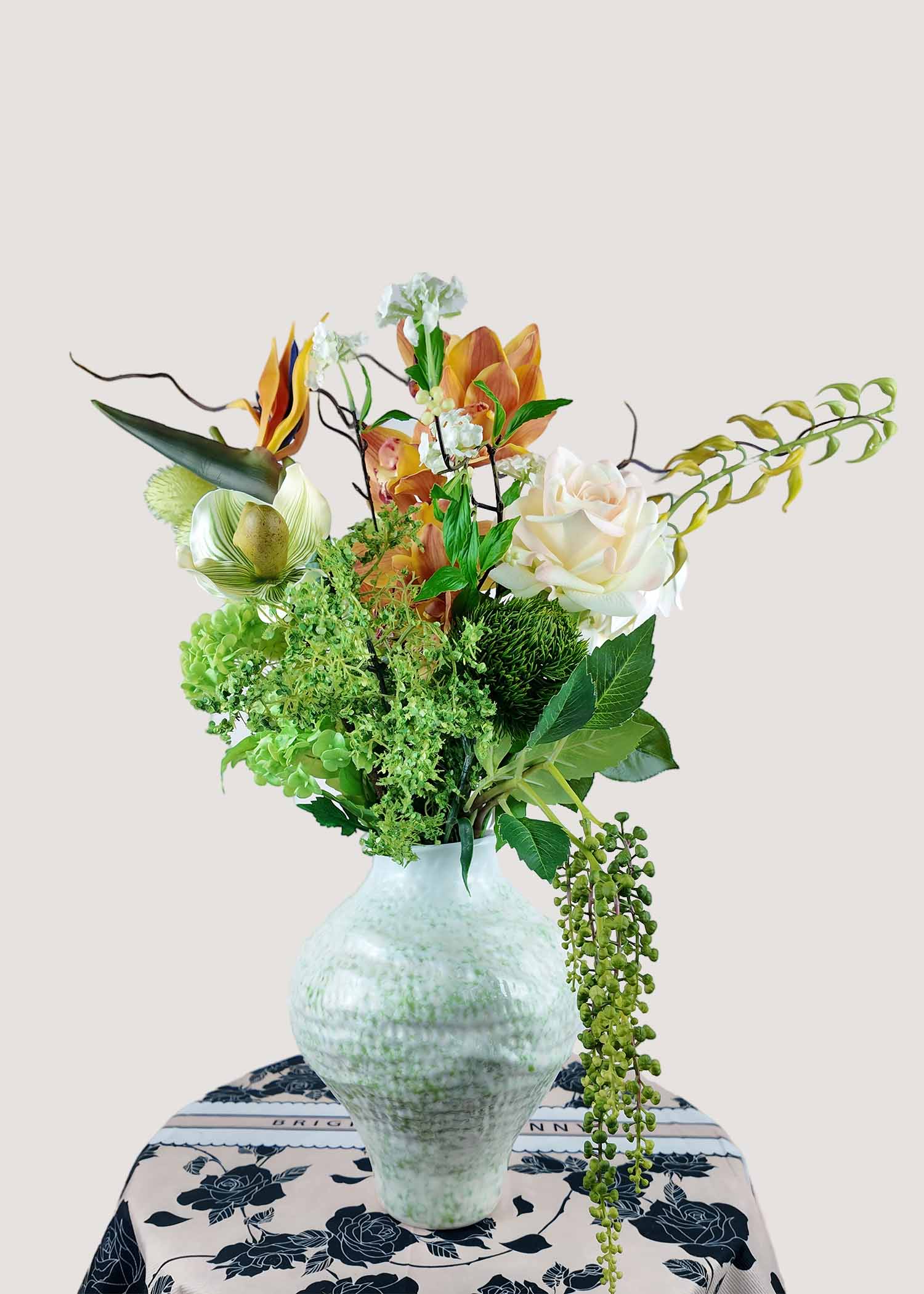 Luxury faux floral arrangement with bird of paradise, orchid, jasmine, hydrangea, balloon pods, and cascading greenery in vase.