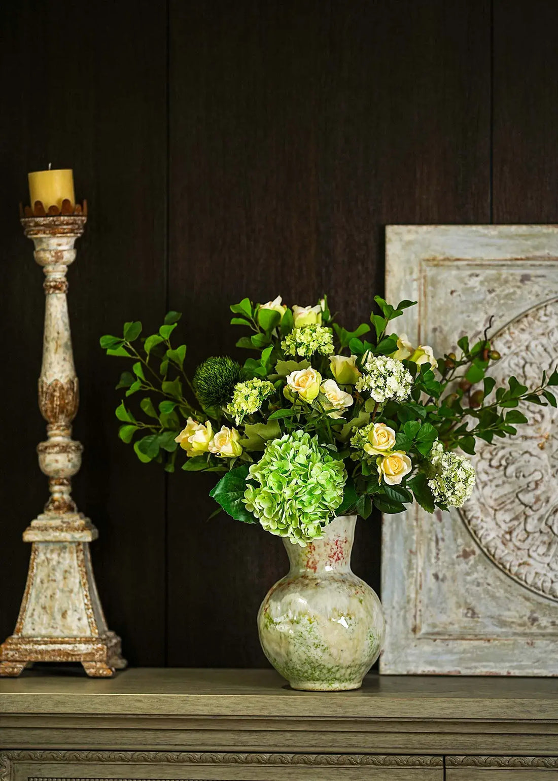 Everblooma faux floral arrangement with green hydrangea and white roses styled against a dark wood background with candle stand.