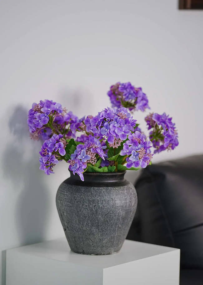 Lavender artificial hydrangeas bouquet in matte black vase on white side table, minimalist living room decoration