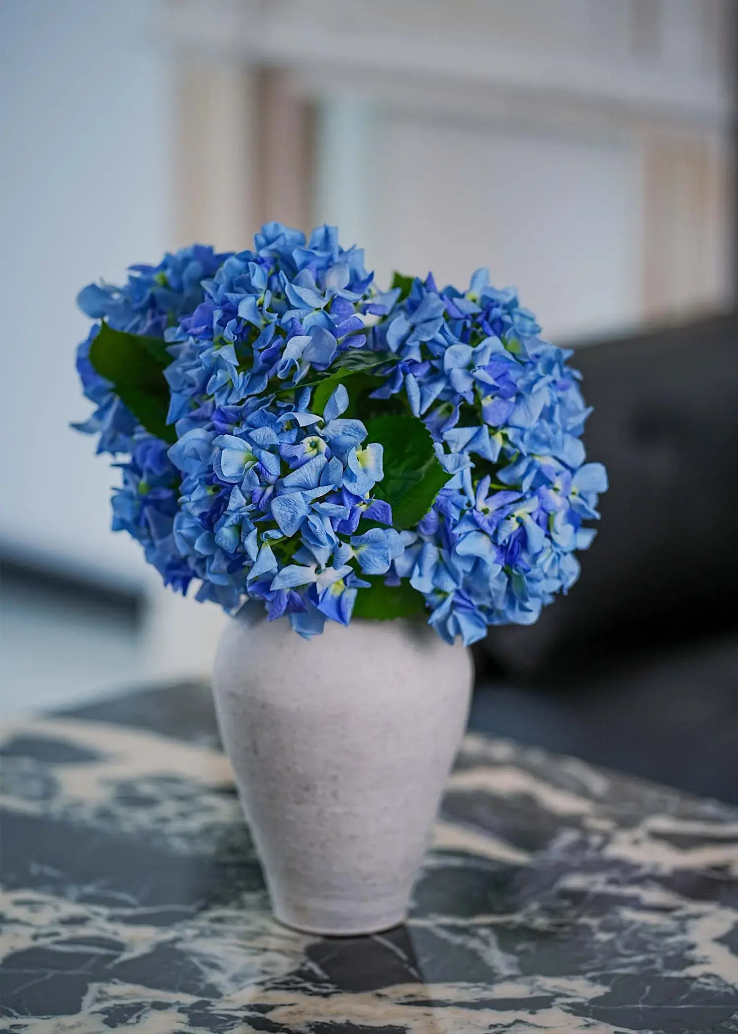 Close-up of silk blue hydrangea petals showing lifelike detail and natural leaf texture in artificial flower arrangement