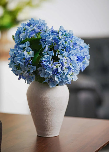 Everblooma sky blue artificial hydrangeas in white ceramic vase, side angle showcasing realistic faux flower texture