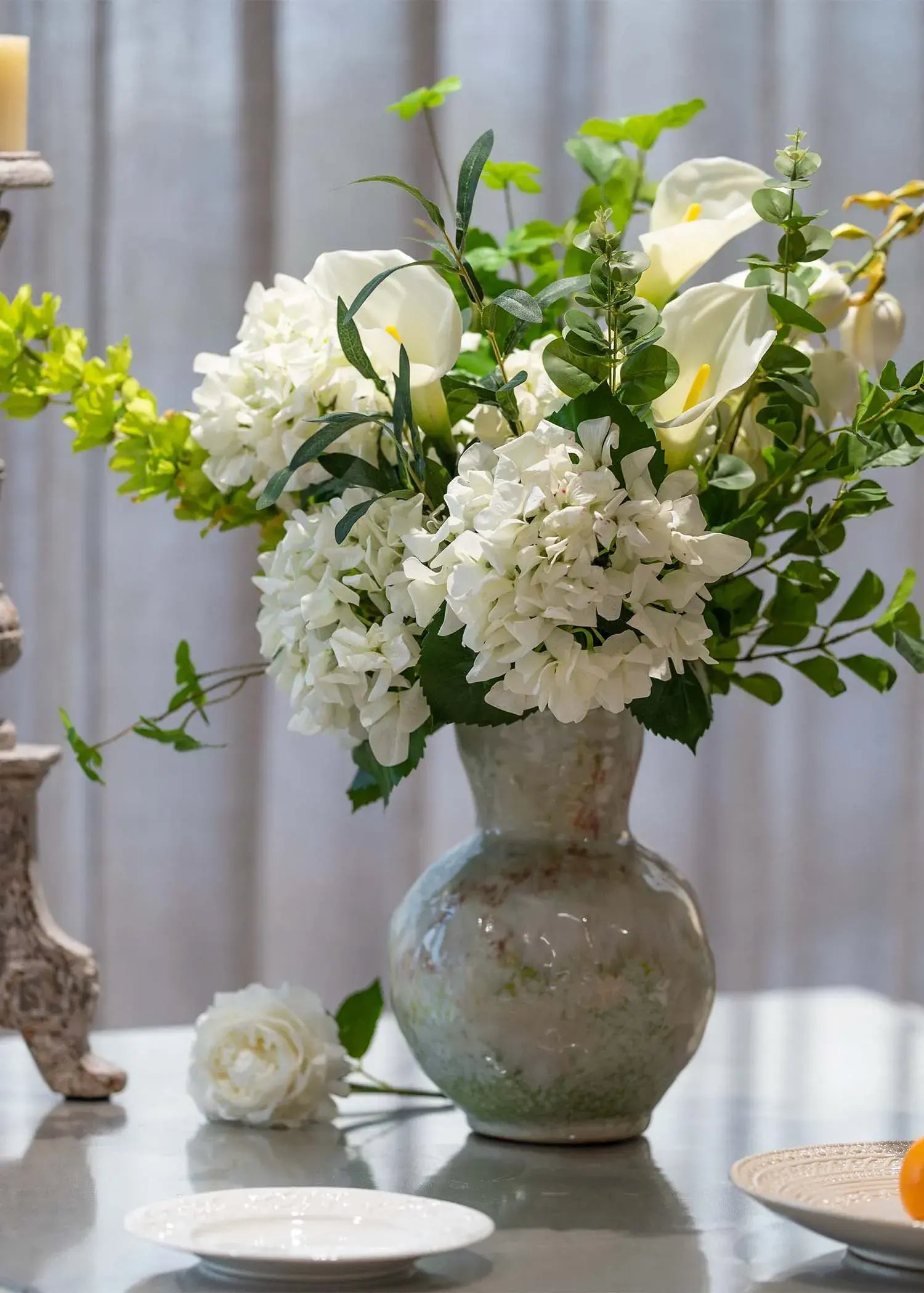 White and green artificial flower arrangement featuring hydrangeas, eucalyptus, and olive leaves displayed on a dining tabletop – Everblooma faux florals