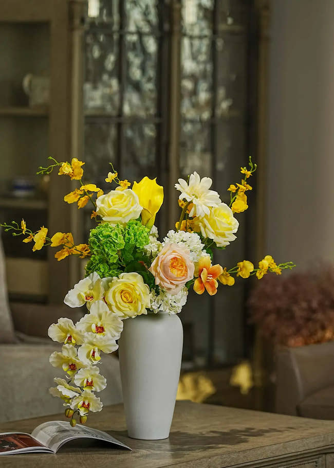 Real Touch faux floral centerpiece with roses and orchids arranged in a tall white vase, styled on a wooden table in a cozy living room — Everblooma home décor.