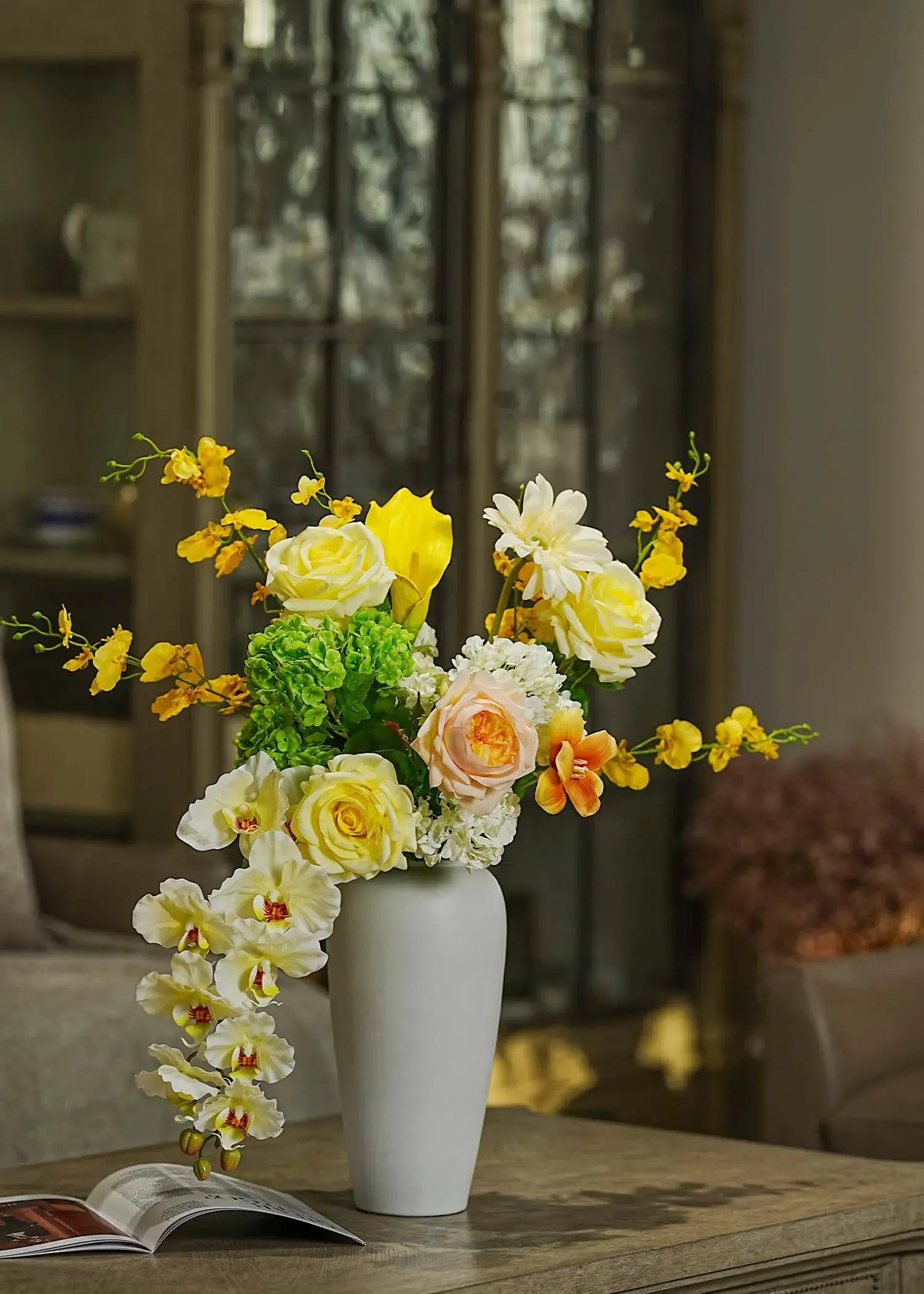 Real Touch faux floral centerpiece with roses and orchids arranged in a tall white vase, styled on a wooden table in a cozy living room — Everblooma home décor.