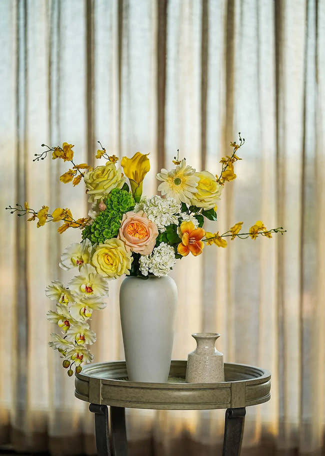 Real Touch faux floral centerpiece with roses and orchids in a tall white vase, styled on a round table with soft curtain backdrop — Everblooma elegant home décor.