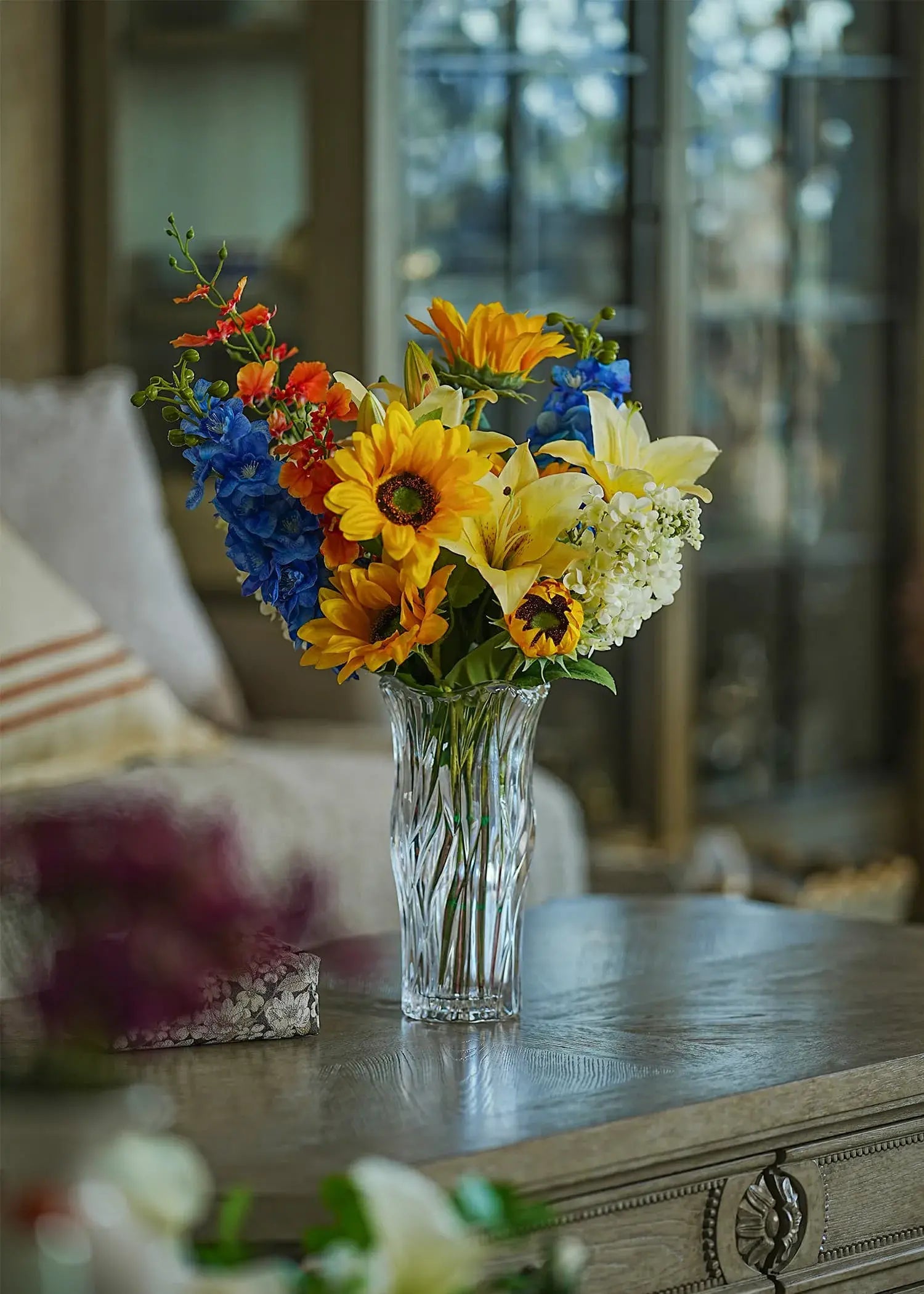 Sunlit Meadow faux sunflower and lily bouquet in a clear glass vase displayed on a wooden coffee table in a cozy living room.