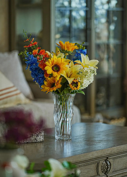 Sunlit Meadow faux sunflower and lily bouquet in a clear glass vase displayed on a wooden coffee table in a cozy living room.