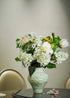 White hydrangea and peony faux floral arrangement in a green ceramic vase placed on a dining table, elegant and natural home décor centerpiece.